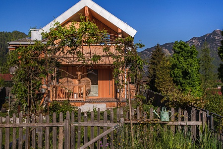 Ein charmantes Chalet mit einer Holzveranda, umgeben von einem gepflegten Garten und Bergen im Hintergrund, bei den Alpegg Chalets