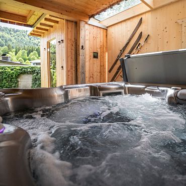 Außenbereich eines Whirlpools bei den Alpegg Chalets mit Blick auf grüne Wälder und Berge