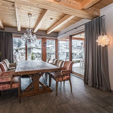 Gemütlicher Essbereich mit Altholztisch und Stühlen vor einem großen Panoramafenster mit Ausblick auf die Tiroler Alpen