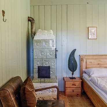 Ein Schlafzimmer mit einem traditionellen Ofen und Holzbett in der Talsenalm