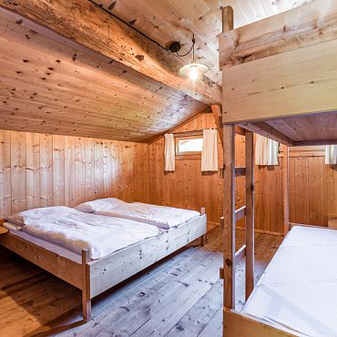 Ein rustikales Schlafzimmer mit Doppelbett und Etagenbett aus Holz in der Talsenalm